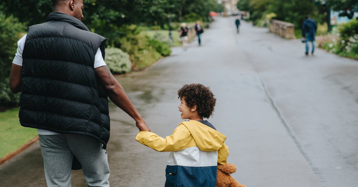 If Bruce Wayne's father was the richest person in city, how was he alone with his child and wife on a road without a driver or bodyguard? - Back view of anonymous African American man holding cheerful son by hand while looking at each other on urban road
