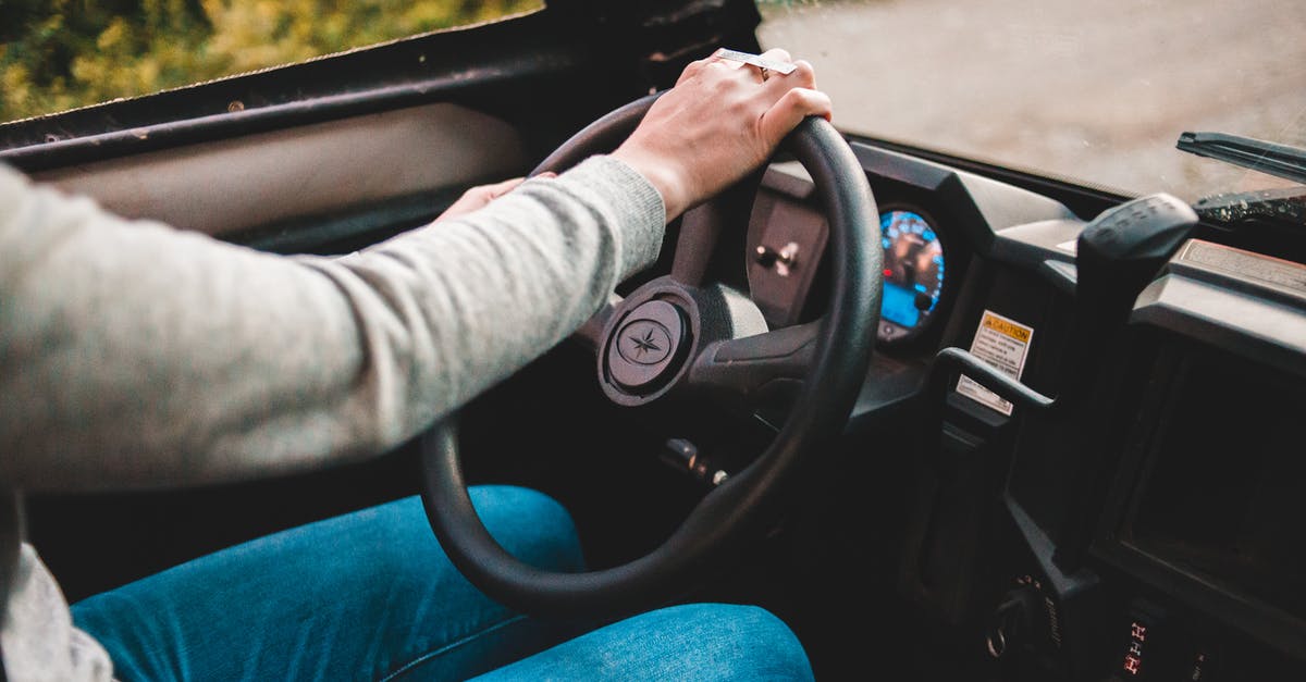In Cabin in the Woods, why does he start the car with his left hand? - Faceless driver in grey sweater and jeans using big black round spinning wheel while driving automobile in countryside