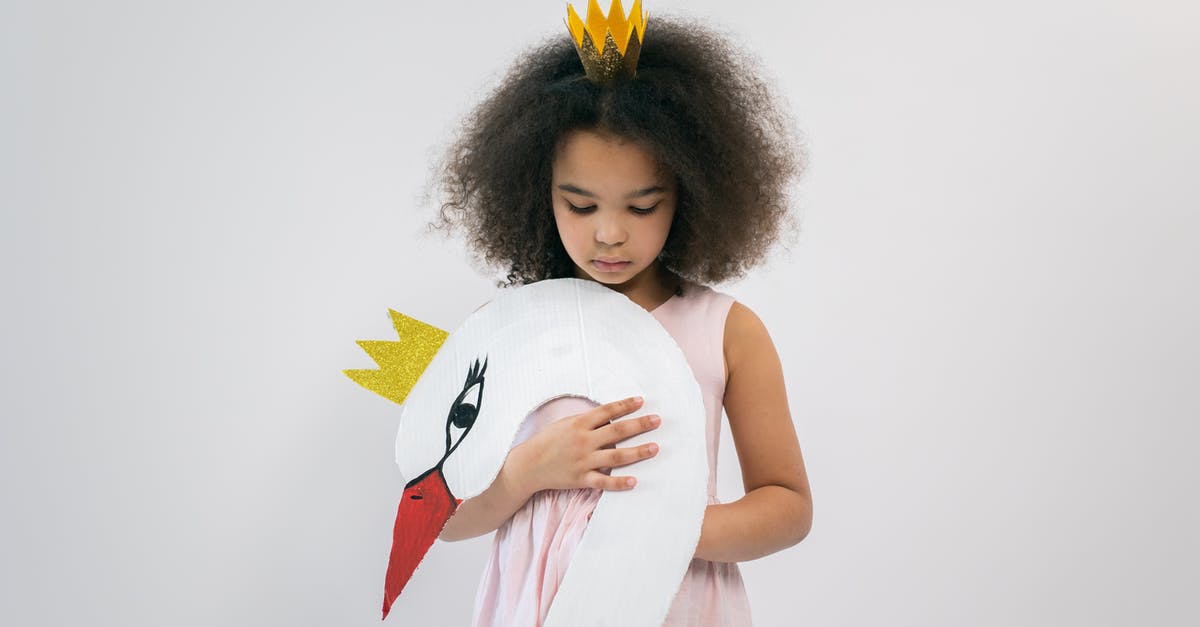 In Disney’s Cinderella, is her full name Princess Cinderella Charming? - Cute African American child in pink dress and crown holding paper swan with crown while looking down and standing on white background in studio