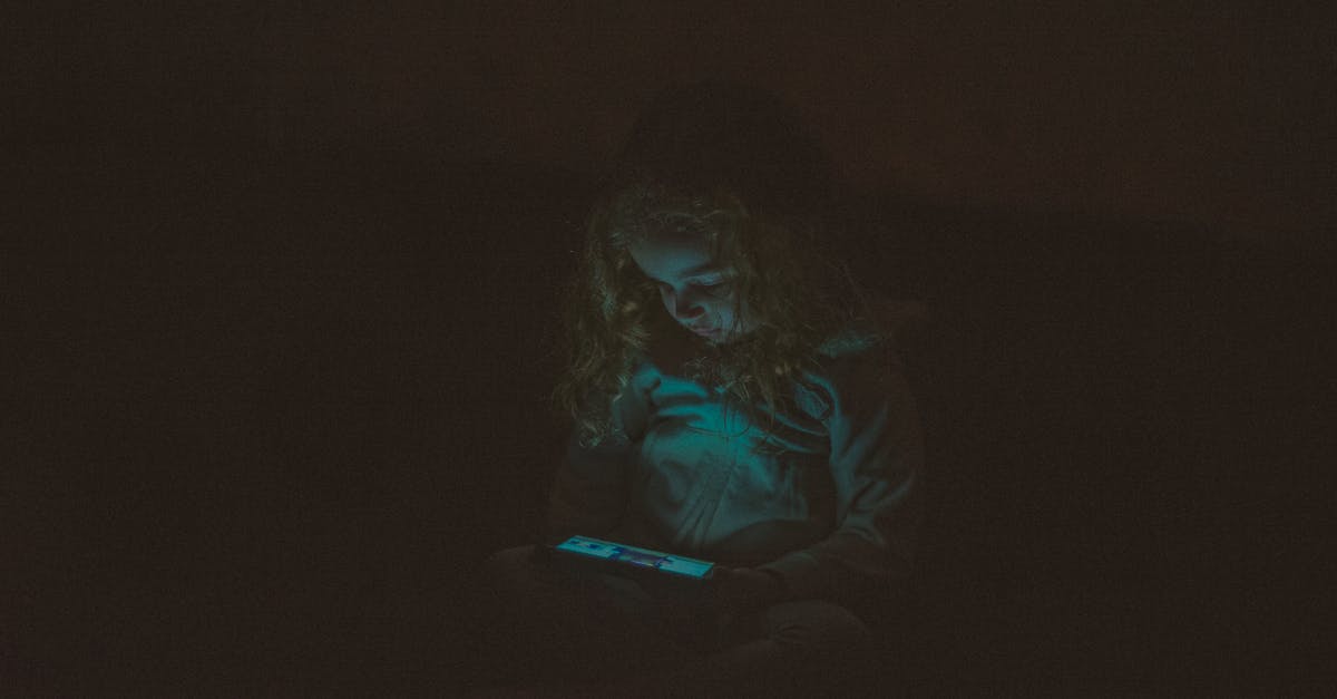 In Night Watch what is the gloom? - Focused  little girl with long curly hair in casual clothes sitting and using smartphone while watching video in dark room
