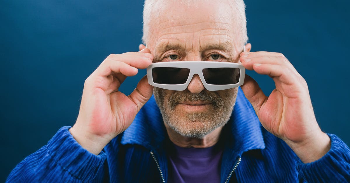 In old films, why do characters flail around when they're shot? - Confident bearded senior gray haired male in blue jacket and sunglasses standing against blue background and touching glasses while looking at camera