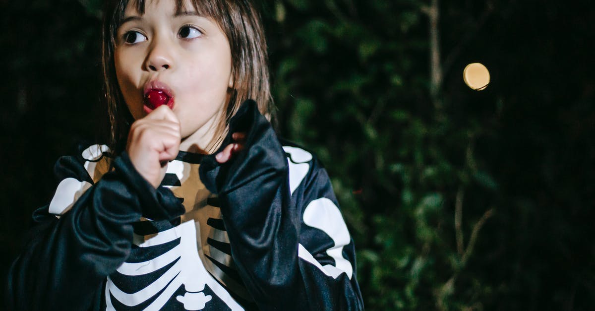 In the American version of The Girl With the Dragon Tattoo, was the falling water-bottle an accident? - Crop contemplative girl in skeleton costume eating delicious lolly while looking away during festive occasion in park in twilight