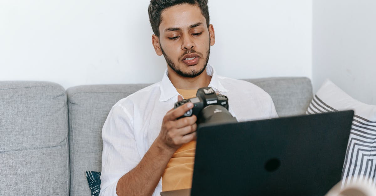 In what year is The Art of Self-Defense set? - Young bearded ethnic male photographer checking pictures on photo camera while sitting with laptop on sofa and working on freelance project