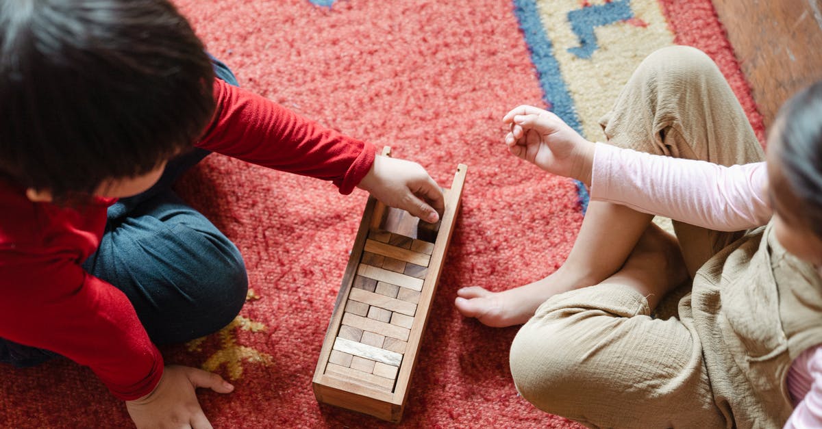 Is Brick Tamland from the future? - From above of anonymous barefoot boy and girl in casual clothes sitting on floor carpet and playing with wooden blocks of jenga tower game