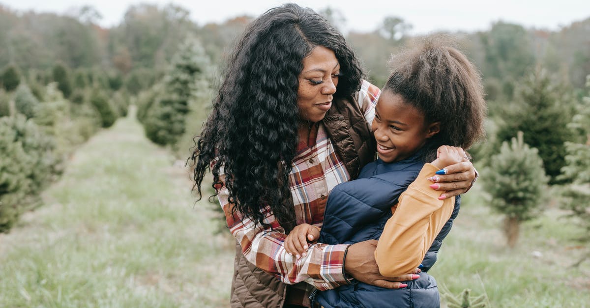 Is Eve or Margo Nick Marshall's mother? - Cheerful African American mum cuddling child while standing close among rows of Christmas trees