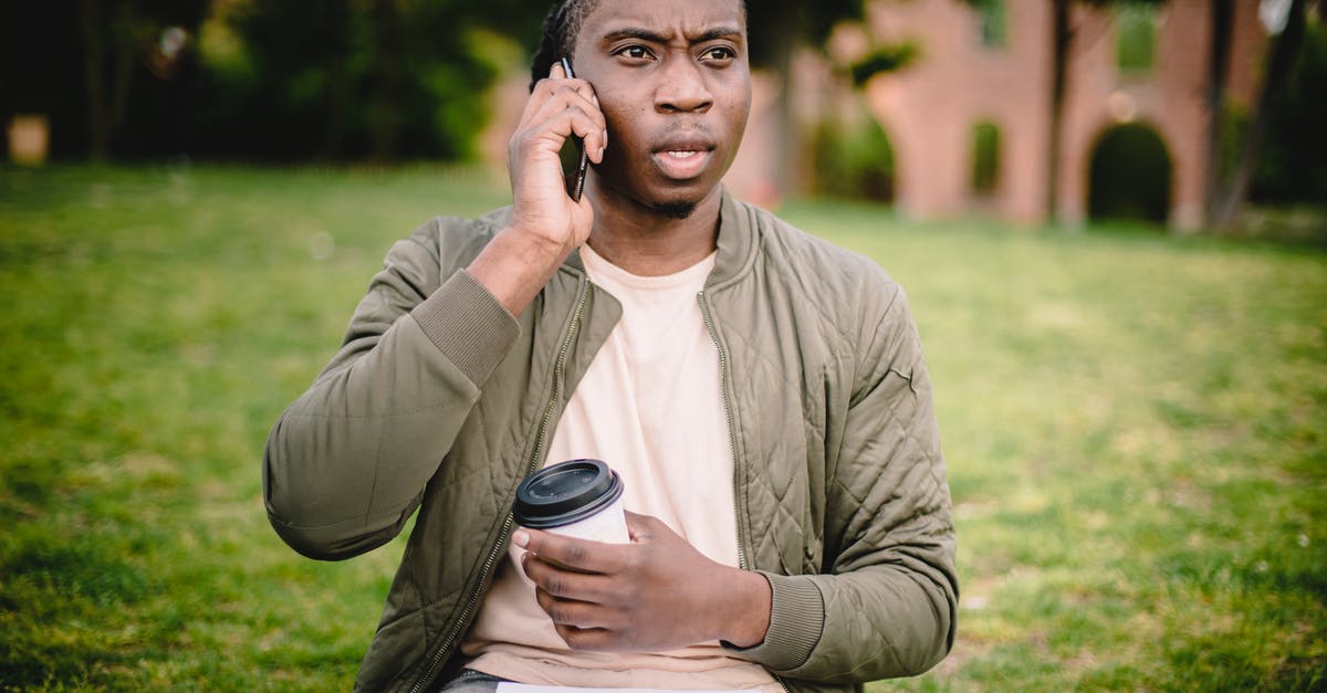 Is Harrison really a bad guy? - Young African American male in casual clothes with cup of coffee to go in hand talking on mobile with expression of displeasure and misunderstanding on face while sitting in park