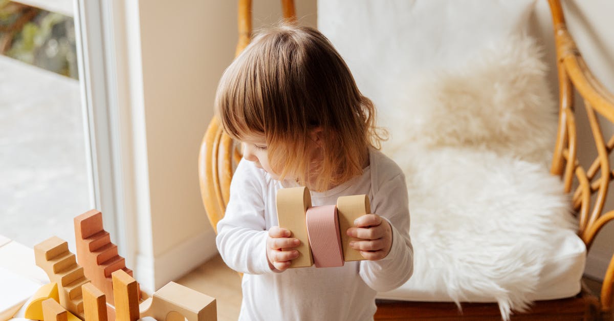Is it legal to show kids reaching orgasm with clothes on? - From above of cute little child in white wear holding wood blocks for building while standing near wicker armchair