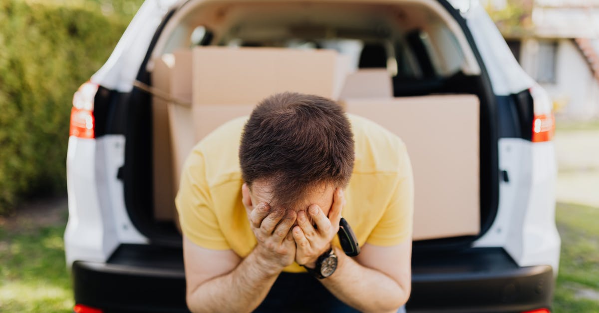 Is man capable of tearing off a car trunk lid as shown in U.N.C.L.E.? - Faceless frustrated tired male wearing casual outfit sitting on car luggage boot and covering face with hands during relocation on sunny summer day