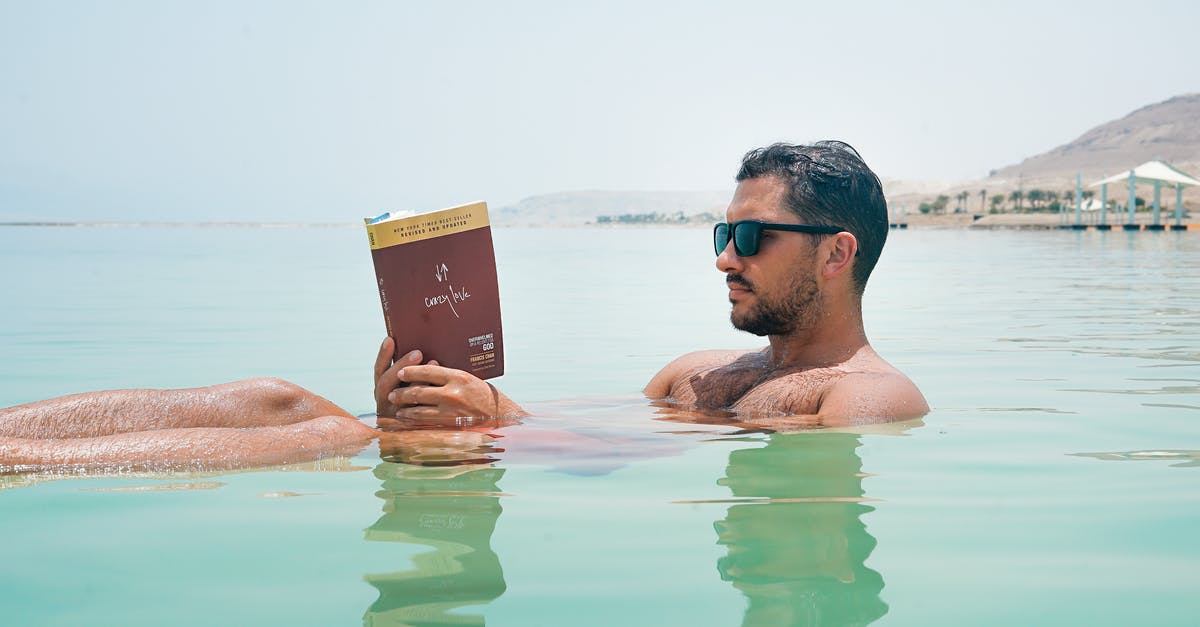 Is Sunshine dead? - Man Wearing Sunglasses Reading Book on Body of Water