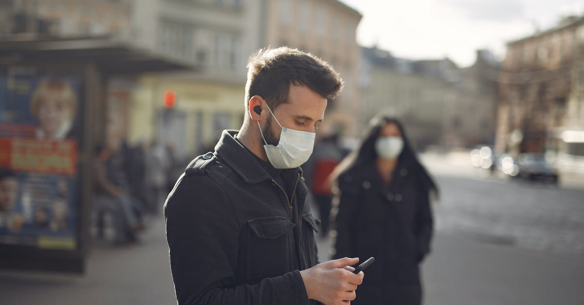 Is the drug used to stop infection in The Rock real? - Focused man in medical mask using smartphone on urban street in cold season