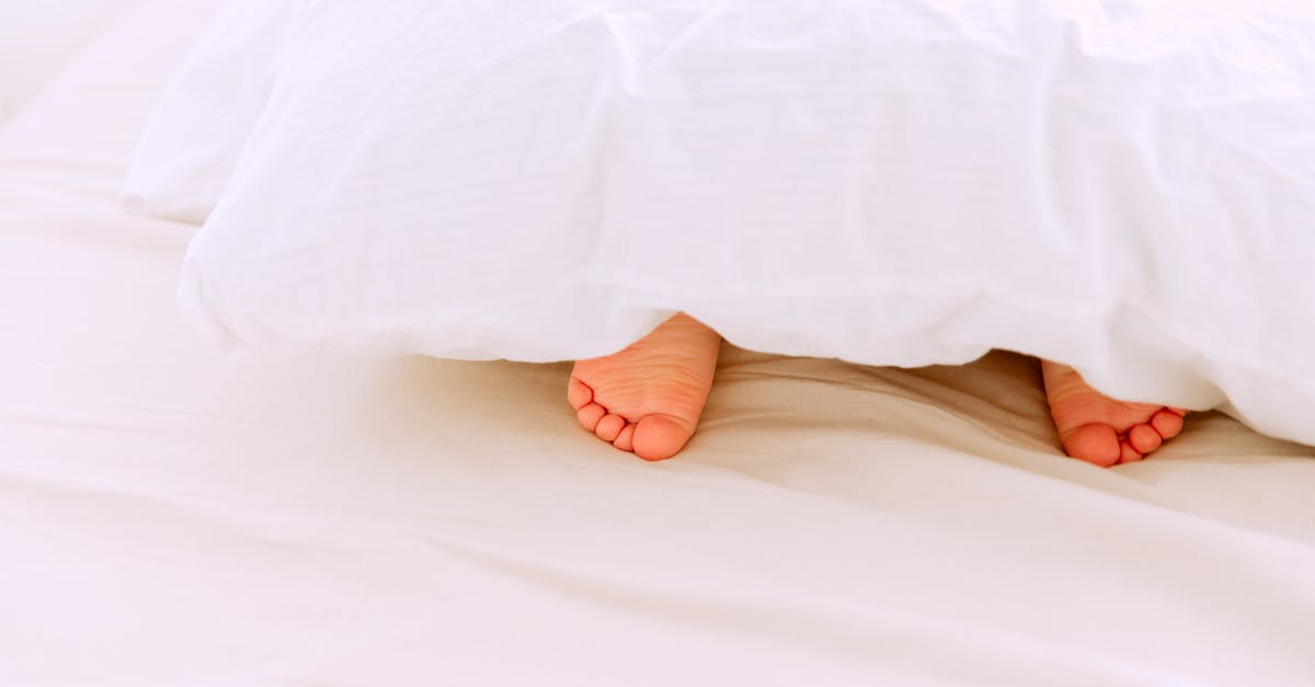 Is the prophet under the thrall of Hades? - Crop tiny feet of little child lying under white blanket on comfortable bed in light bedroom at home