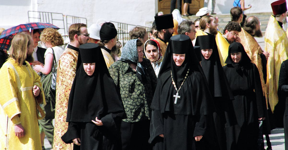 Is the "person defending trailerhome with a shotgun" a common scene? - Nuns of convent wearing black clothes walking along street passing men of cloth in golden color robes and common people located near building celebrating holiday in sunny day