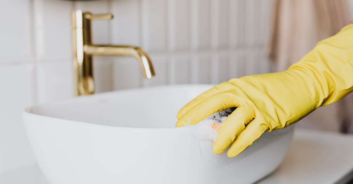 Is there a meaning behind the dripping sink at the end of the movie? - Crop faceless person in yellow latex protective glove cleaning surface of white stylish sink in contemporary bathroom interior