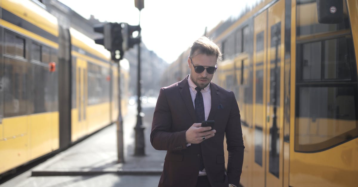 Is there an alternate version of "Duel" where the truck stands waiting for the guy after the train has passed by? - Brutal male entrepreneur in elegant suit and sunglasses standing with hand in pocket on street between trams and messaging on cellphone