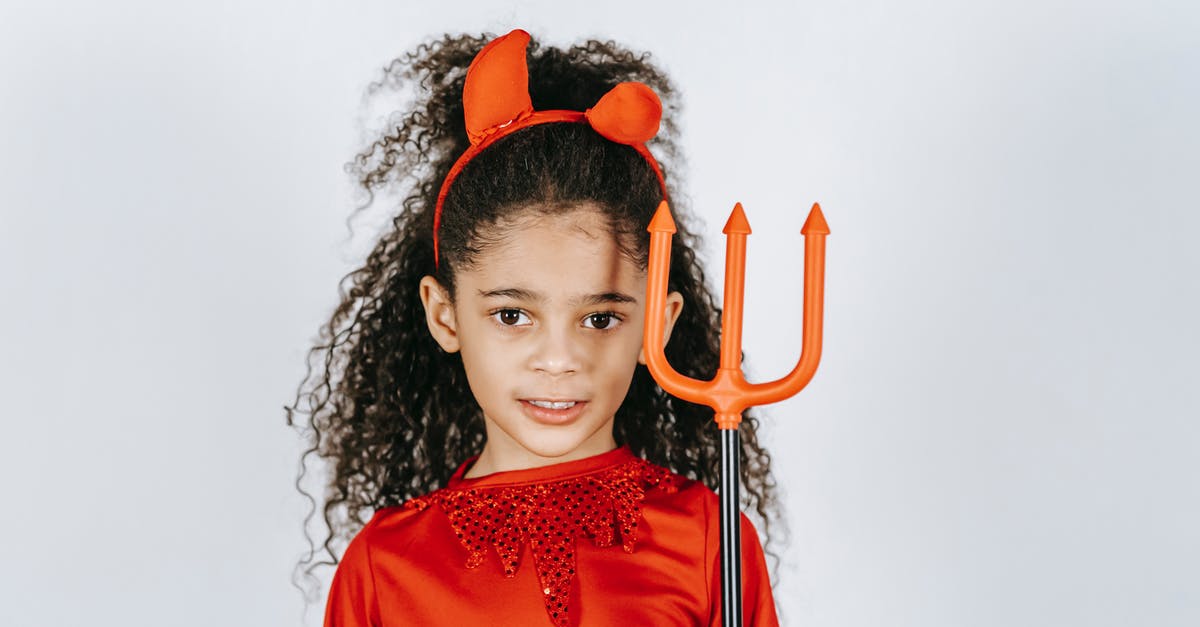 Is this character supposed to be the Devil? - Adorable African American child with long curly hair showing artificial trident while standing in white studio in red Halloween costume of devil