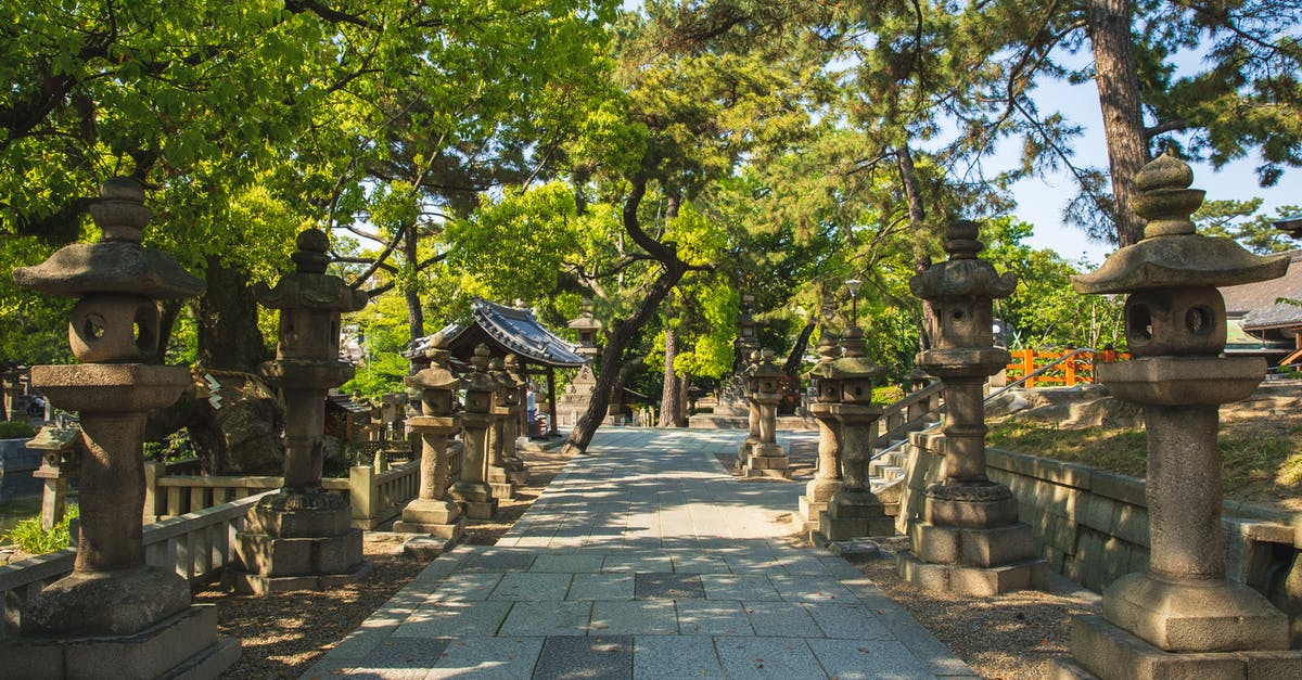 Is this Green Lantern and Batman reference intended for a Justice League movie? - Traditional stone lanterns installed on aged columns near calm walkway located under high trees in Japanese park on sunny day