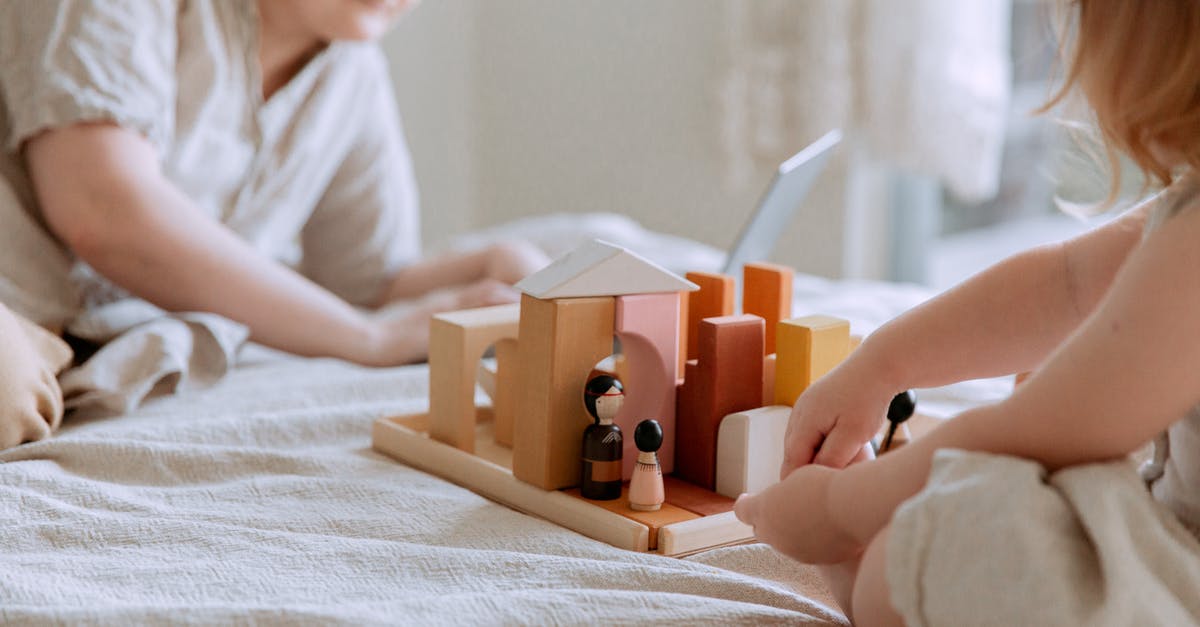 La Pianista - why did she break the girl's hand? - Faceless toddler girl sitting on bed and playing with wooden blocks and toys while mother using laptop