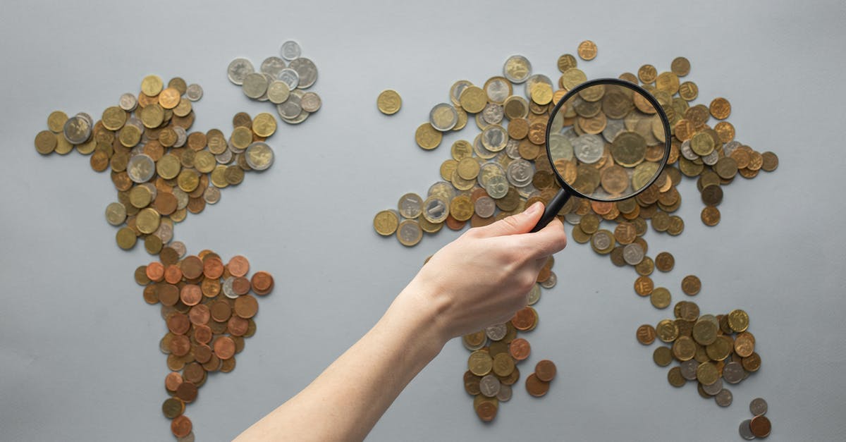 Lighting mismatch in "All the Money in the World" - Top view of crop unrecognizable traveler with magnifying glass standing over world map made of various coins on gray background