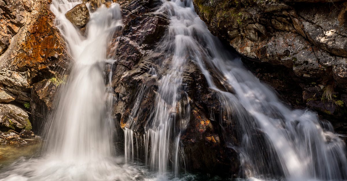 Location of the scene with the river and waterfall: is the waterfall a joining of two streams? - Long exposure of rapid cascade falling from rough rocky cliff into foamy splashing river in wild nature with stony formations