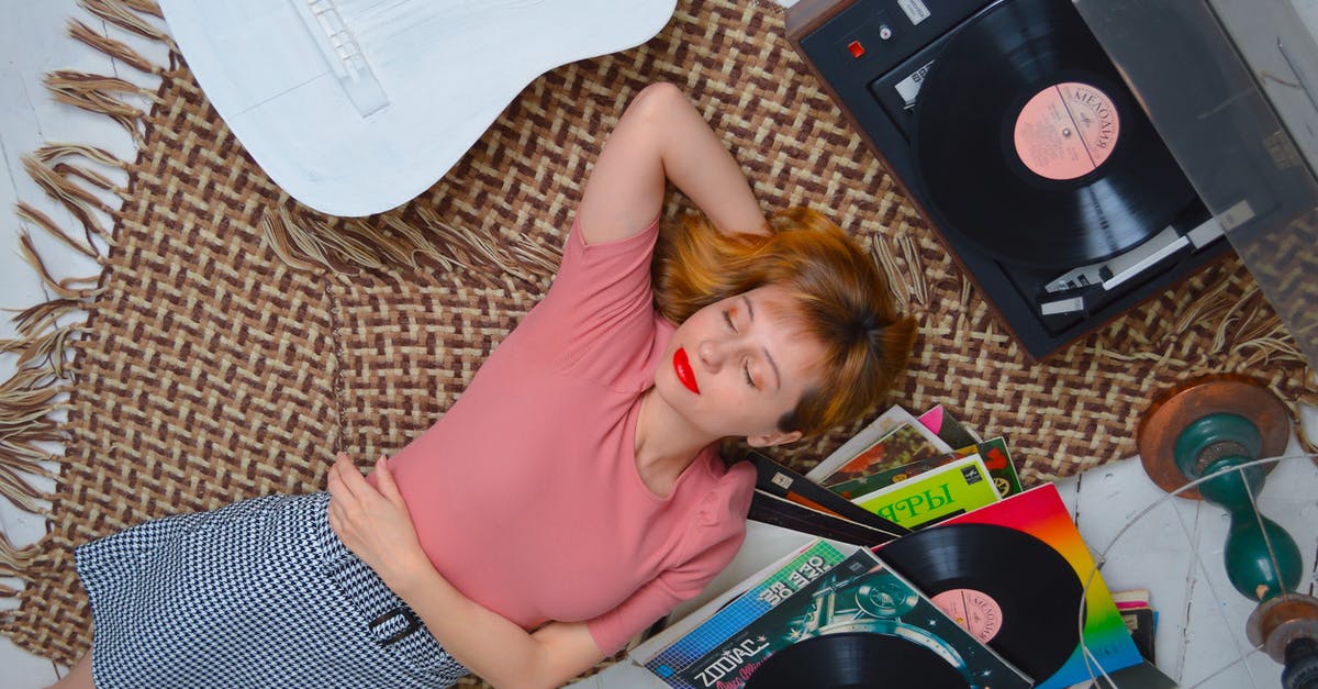 Music player device from Star Trek Beyond - Top view dreamy young female with red lips wearing casual wear lying on floor with eyes closed and hand behind head and listening to vinyl record player