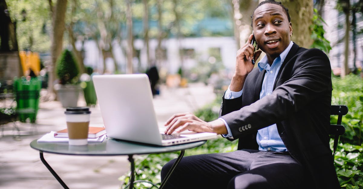 Mysterious Short Hostile Phone Conversation in Training Day - Cheerful young African American male entrepreneur having phone call while working remotely on laptop in street cafe on sunny day