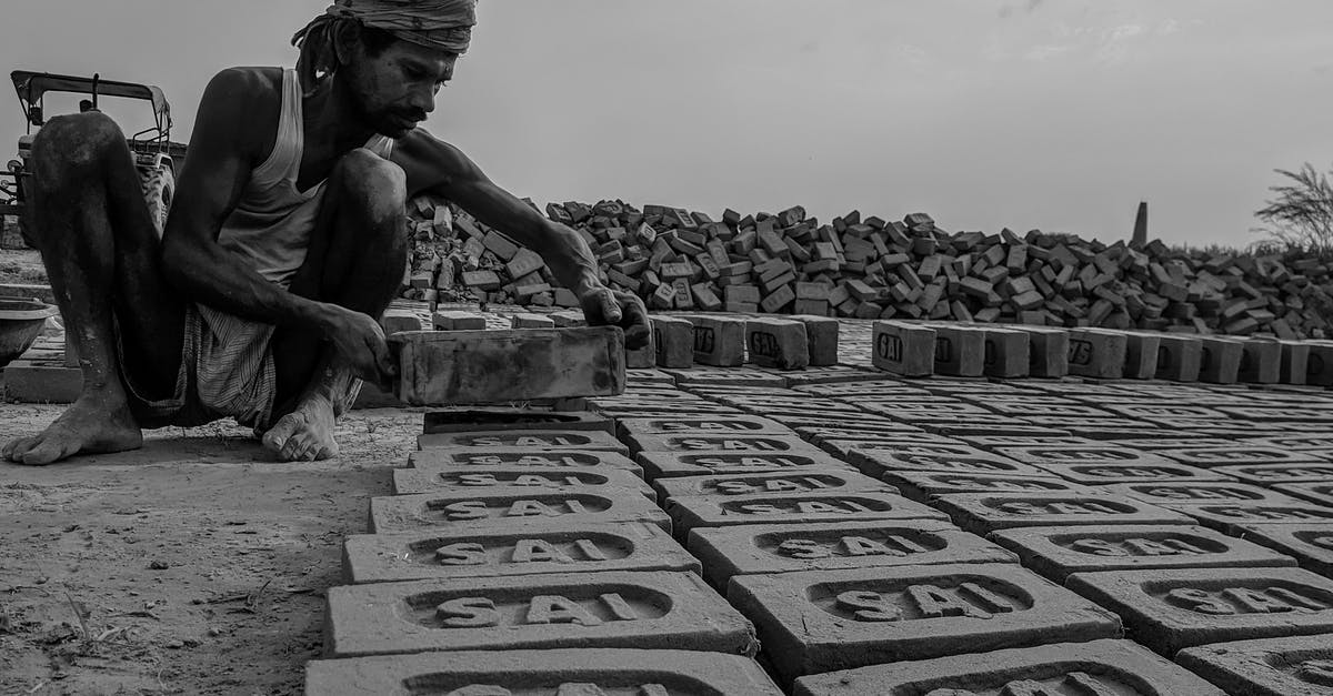 Name of the role that is neither primary nor support, similar to the dodging guy in Mummy Returns? - Black and white ground level of poor barefoot ethnic male in head wear squatting while putting bricks with carved letters on dry terrain