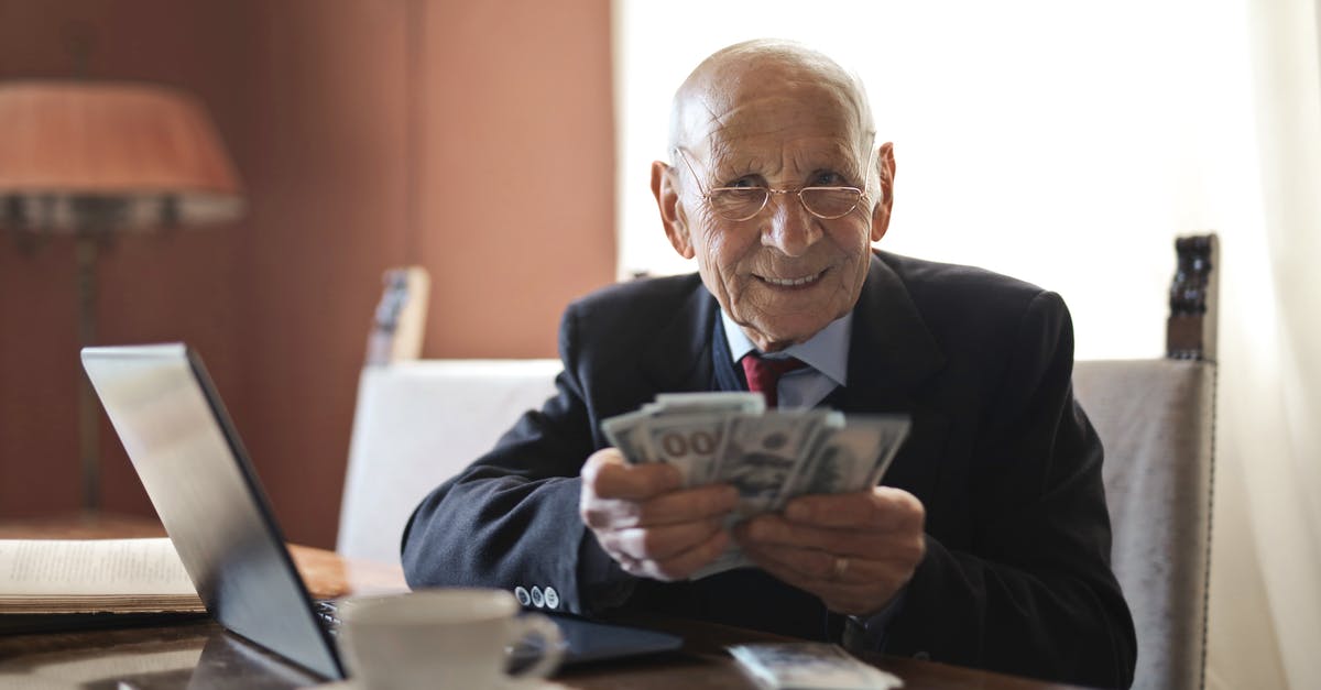 Old Money vs New Money theme - Confident senior businessman holding money in hands while sitting at table near laptop