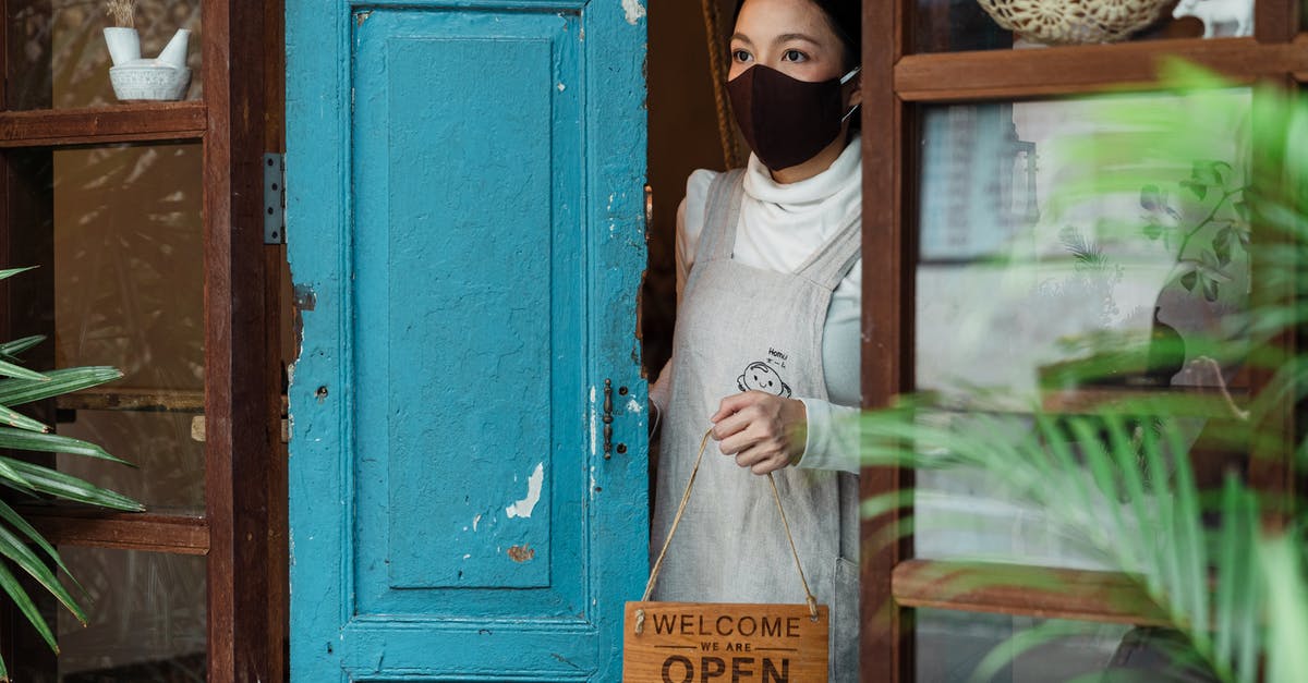 Open vs closed shot - Calm young Asian female wearing casual clothes and face mask standing at shabby rural shop doorway and removing open sing