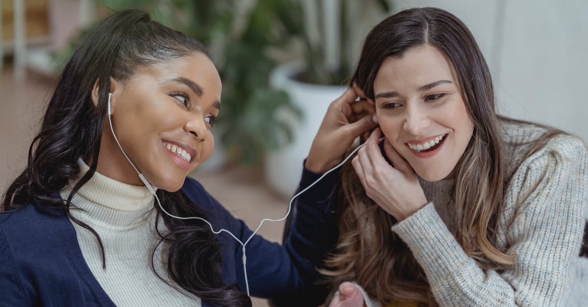 "Highlander" music used as New Line Cinema theme song - Happy young African American lady with smartphone and earphones smiling and sharing music with female best friend while chilling together in cozy cafe