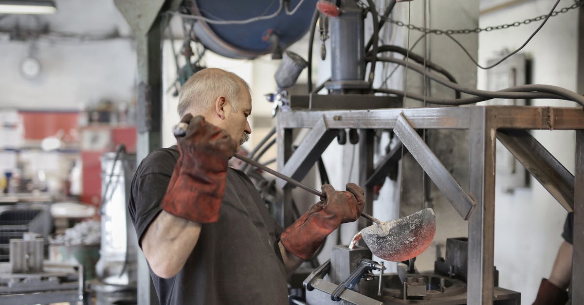 Realism of the responsibilities of the senior staff in the West Wing - Side view of senior white hair worker in apron and heavy duty gloves melting detail from iron