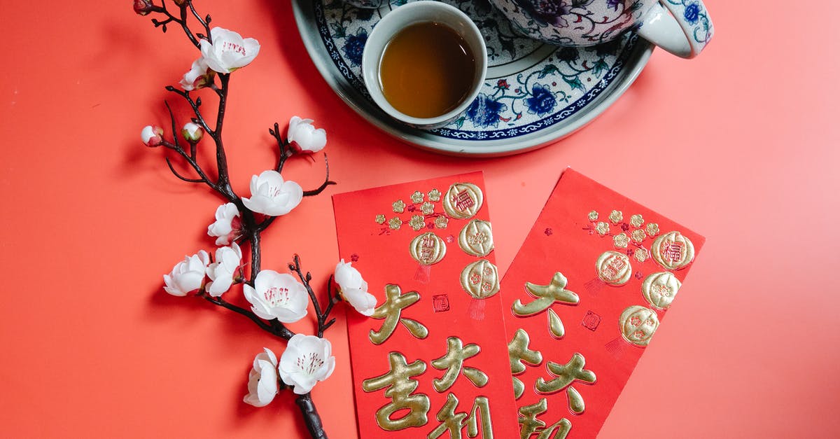 Ritual/symbolism of putting teapot in cup - Top view of oriental packets with hieroglyphs against blossoming flower sprig and tea set during New Year holiday on red background