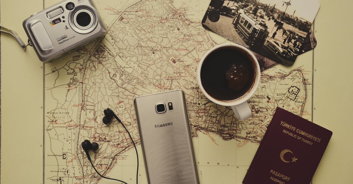 Scene with passport connected to wires - Silver Camera Near Black Coffee in Mug, Silver Samsung Galaxy S7, Turkey Passport, and Black Earbuds