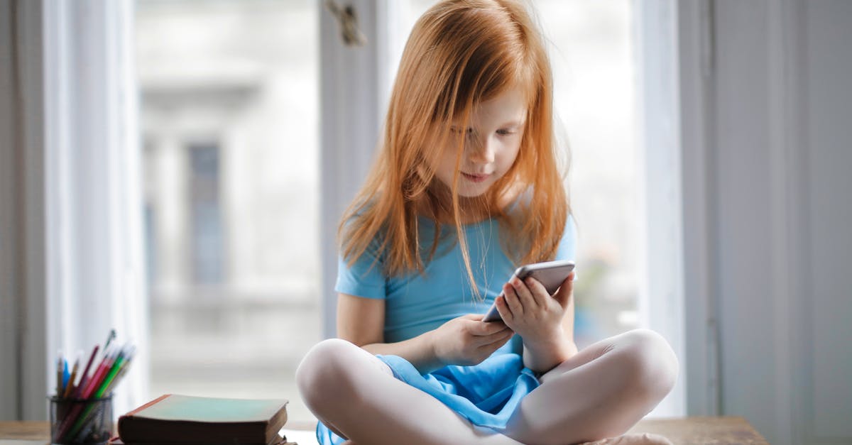 Should I watch Dawn of the Dead before watching Shaun of the Dead? - Red haired charming schoolgirl in blue dress browsing smartphone while sitting on rustic wooden table with legs crossed beside books against big window at home