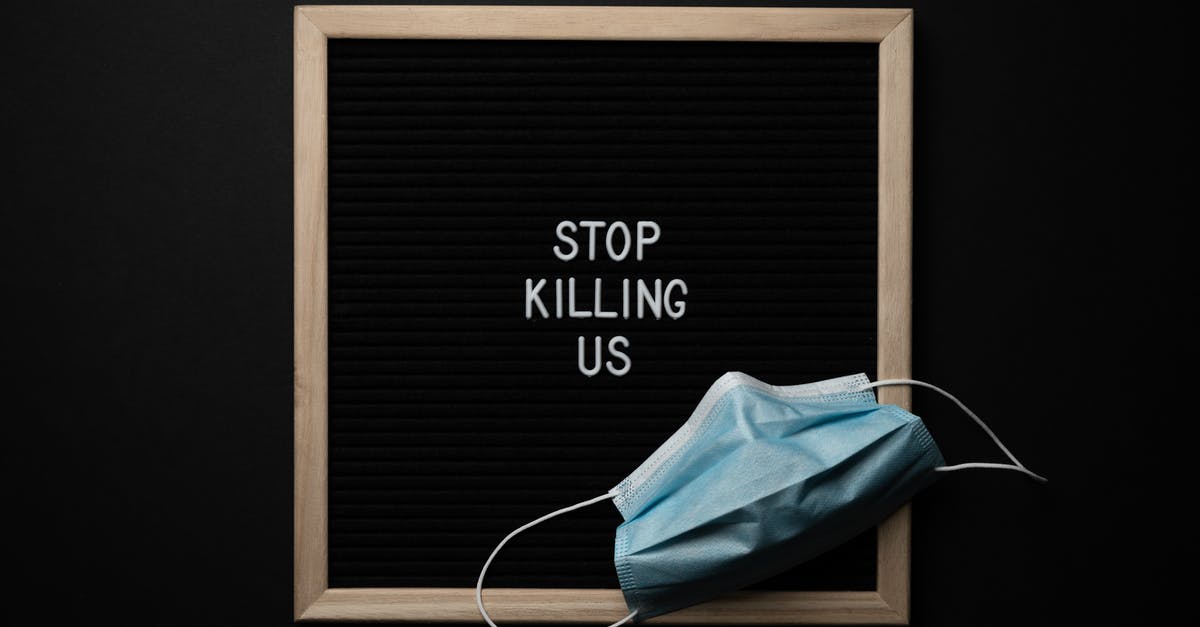 Significance of Dr. Brand's poem - Top view of composition of blackboard with written phrase STOP KILLING US under mask against black background