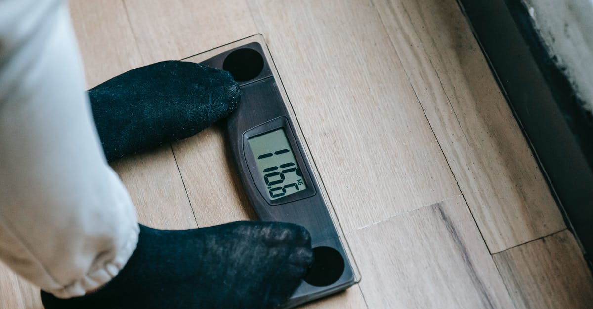 Significance of sacrificing twelve number of people? - From above of unrecognizable person in socks standing on electronic weighing scales while checking weight on parquet during weight loss