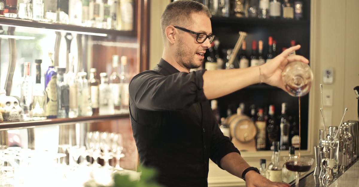 Significance of small wine glass - Side view of positive young barman in black uniform and eyeglasses pouring wine into glass while working at bar counter in modern restaurant