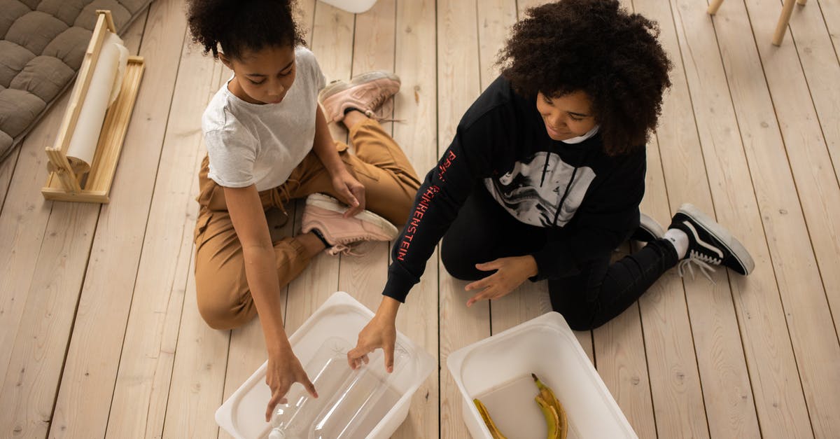 Significance of the difficulty to put bottle in the waste collecting box in all three films - From above full body of African American mother and daughter sorting plastic bottles and banana peel into containers while sitting on wooden floor in room