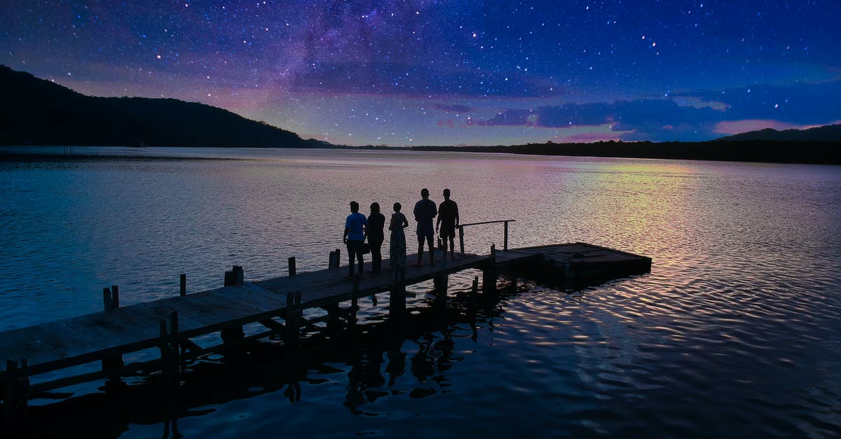 Thanos in Guardians of the Galaxy 2 jump gate scene? - Back view of anonymous people standing on pier near calm rippling lake water under starry Milky Way