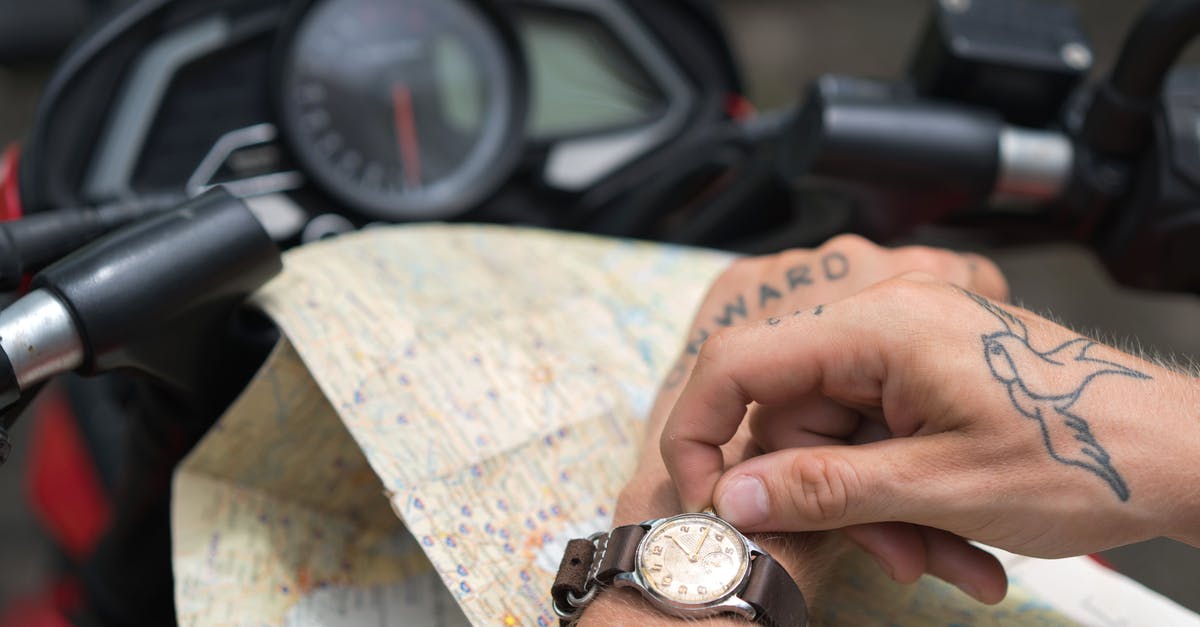 Time and Space Travel? - Crop tattooed man setting up watch against map and motorbike