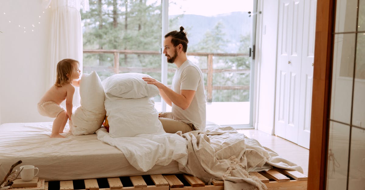Uncle Elroy's bedroom scene? - Side view of serious bearded father in casual clothes playing with little child with pillows on comfortable bed in light bedroom at home