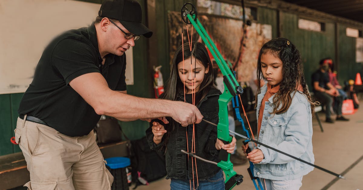 Unwritten rule that you never show a child getting seriously injured or killed? - Adult male archery coach teaching adorable little multiethnic girls to shoot with bow and arrow during classes in range