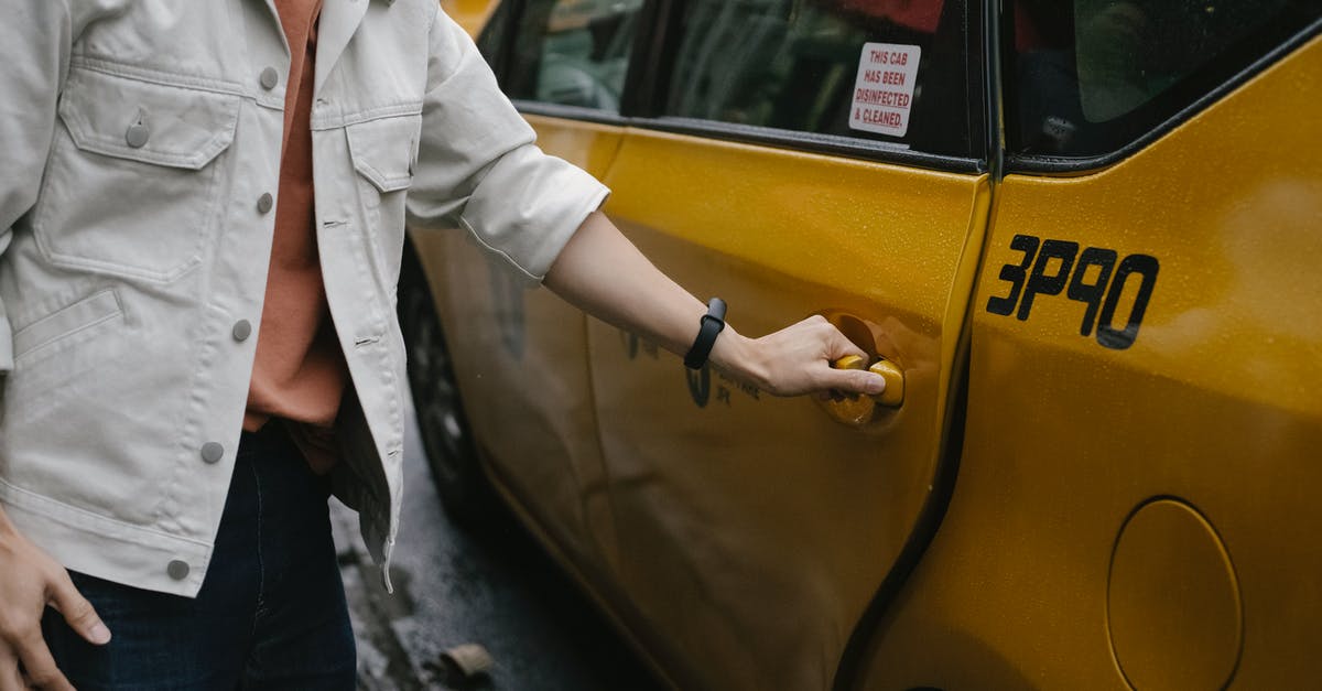 Was it a common practice to pronounce the fare on the cab door in the sixties? - Unrecognizable passenger in casual clothes opening door of cab parked on roadside in city on street while commuting to work