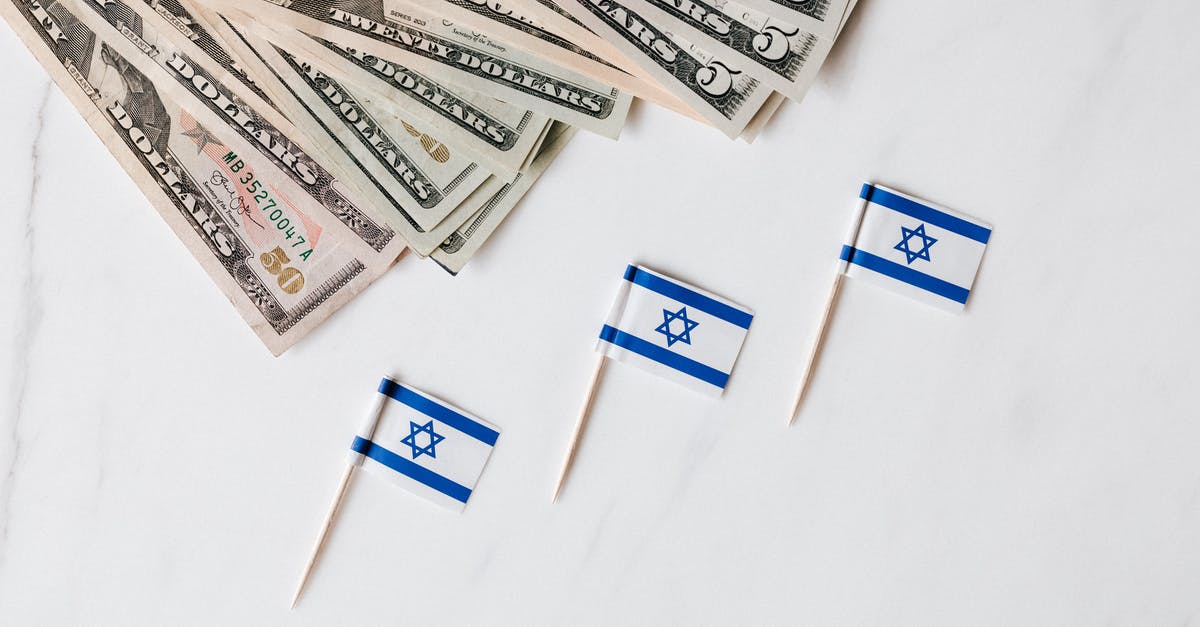 Was there any consideration to set "The Interview" in a fictitious country? - Top view of bundle of different nominal pars dollars and Israeli flags on toothpicks placed on white surface of marble table