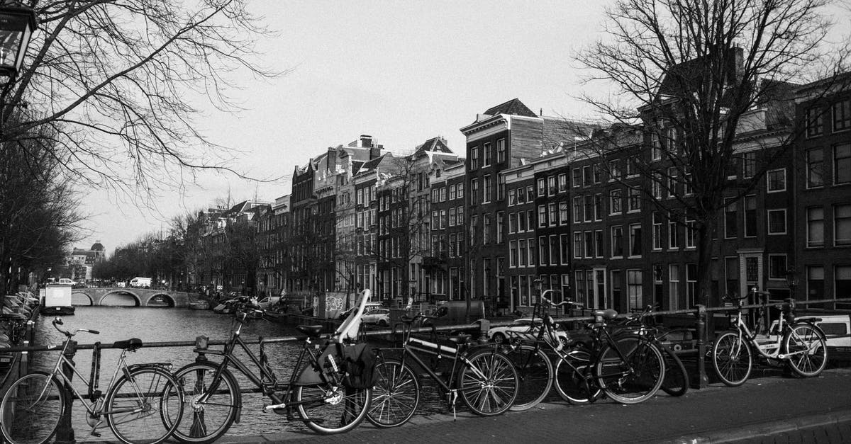 Water as a symbol in Fatal Attraction - Black and white of various bicycles parked on paved bridge over rippling canal near aged typical residential buildings in Amsterdam