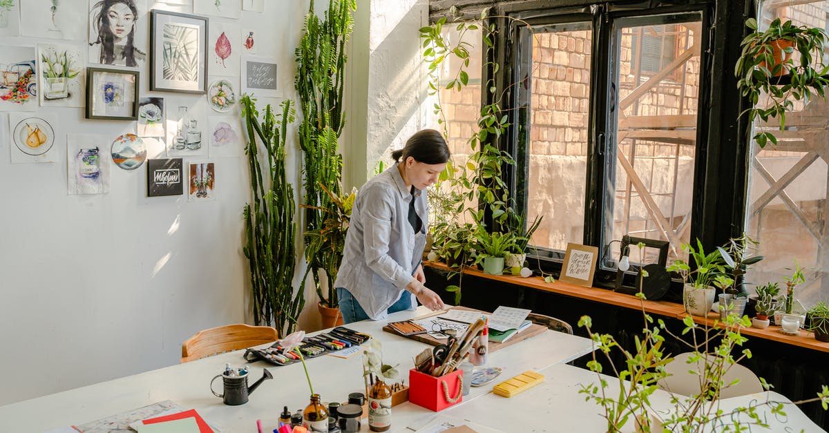 What's the difference between the professional titles "writer" and "screenwriter"? - Side view of female designer creating drawings at desk with collection of felt pens and papers near wall with artworks and plants on windowsill in daylight