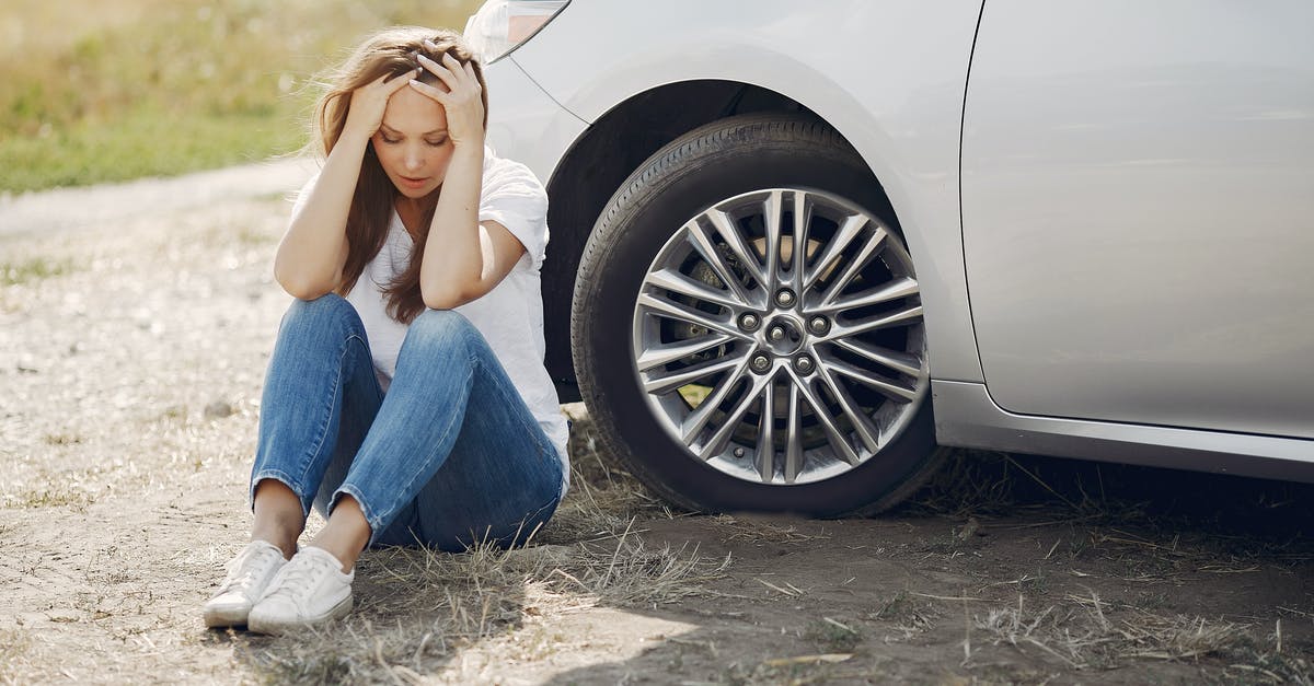 What did the aliens need help for? - Frustrated female driver in white t shirt and jeans sitting on ground near damaged car with hands on head during car travel in sunny summer day