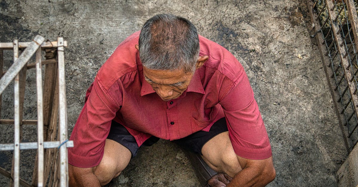 What do I need to see before Spider-Man: Far From Home? - From above of anonymous ethnic male squatting on dirty floor near grid on street in poor district of rural area
