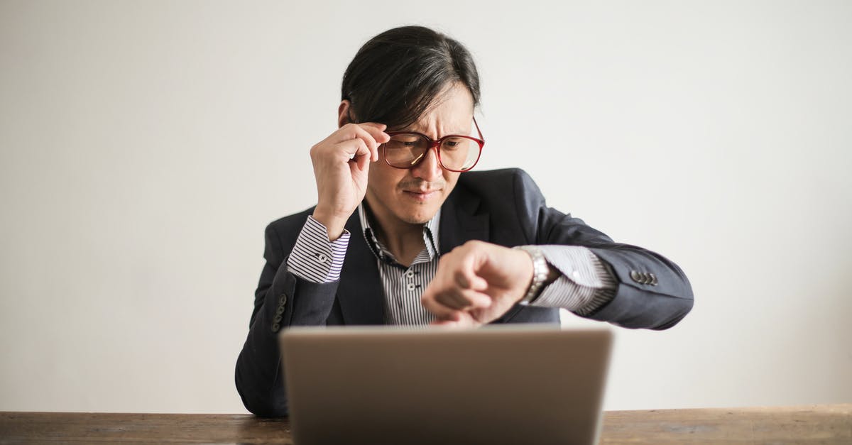 What do the Asian women in bathing suit holding fishes pictures on Molly's computer mean? - Young frowning man in suit and glasses looking at wristwatch while waiting for appointment sitting at desk with laptop