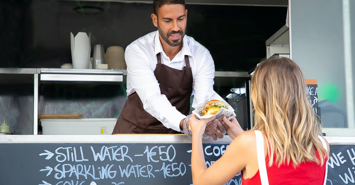 What does Mattingly give Parker? - Positive ethnic cook in apron standing at counter in food truck and giving delicious hamburger to anonymous woman customer in daytime