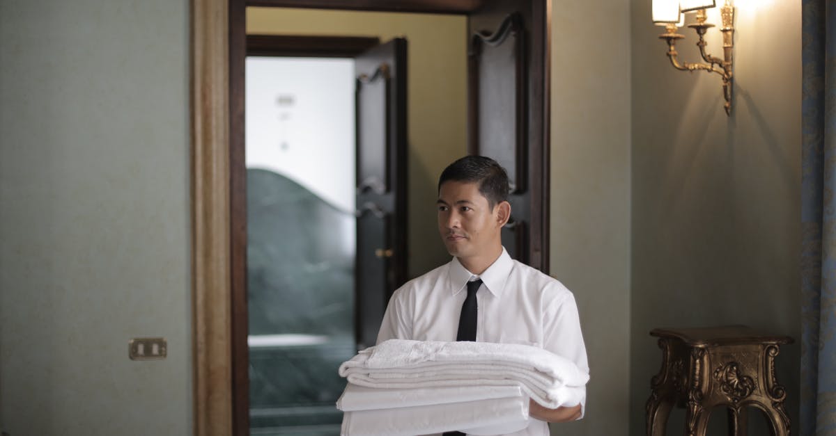 What does the maid mumble? - Young male housekeeper carrying stack of white bed sheets while entering bedroom in hotel